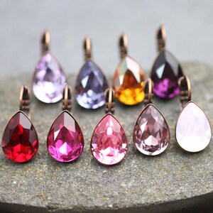 Puede incluir: Surtido de ocho colgantes de cristal en forma de lágrima con un aro de metal de tono cobre. Los cristales son de varios colores, incluyendo rojo, rosa, morado y transparente.