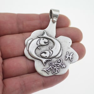 May include: Silver pendant featuring a stylized depiction of two fish, the astrological symbol for Pisces, and a decorative floral design.