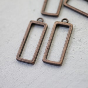 May include: Four antique copper-toned metal rectangular picture frames with a loop at the top for hanging.
