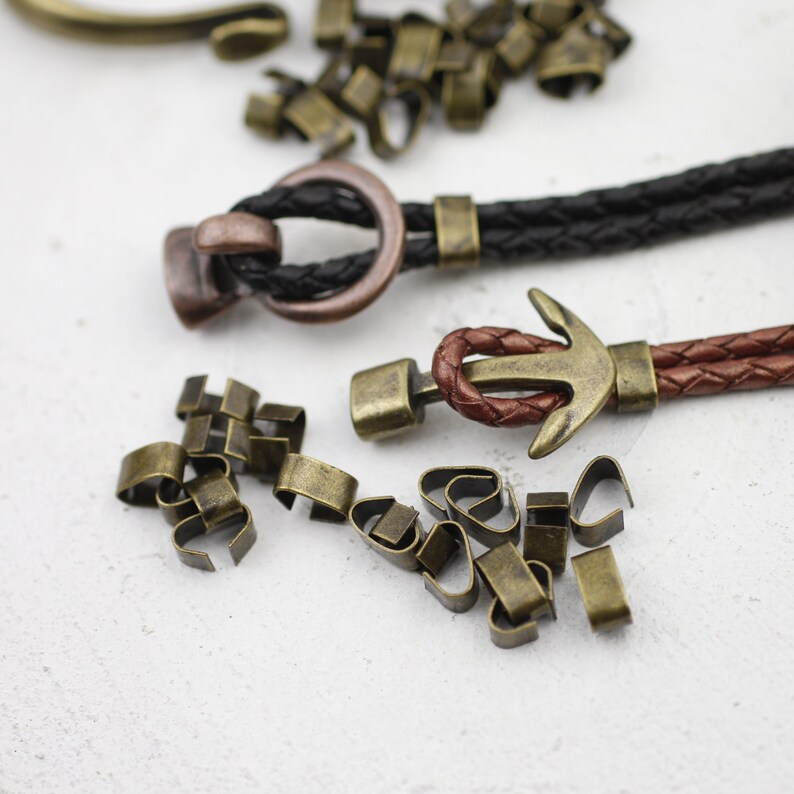 Peut inclure: Gros plan sur deux bracelets en cordon de cuir avec des fermoirs m&eacute;talliques. Un fermoir est une simple boucle, l'autre est un motif d'ancre. Un tas de petits anneaux de saut en m&eacute;tal sont dispers&eacute;s autour des bracelets.