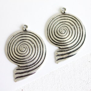 Peut inclure: Deux breloques pendantes en argent en forme de spirale avec une surface texturée. Chaque breloque a une boucle en haut pour l'attacher à un collier ou un bracelet.