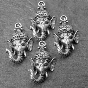 May include: Four silver-toned metal charms featuring the face of the Hindu deity Ganesha. Each charm has intricate details and a raised Om symbol on the forehead.