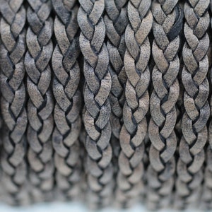 Peut inclure: Gros plan d'un cordon en cuir tressé de couleur brun foncé. Le cordon est composé de plusieurs brins de cuir tressés ensemble pour créer un design texturé et durable.