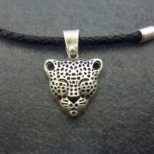 Puede incluir: Collar con colgante de plata con un diseño detallado de cabeza de leopardo. El colgante está unido a un cordón de cuero negro.