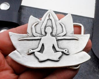 May include: Silver-toned belt buckle featuring a stylized figure in a lotus position, with arms raised above the head.