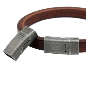 May include: A brown leather bracelet with a silver magnetic clasp. The clasp is made of two pieces that snap together.