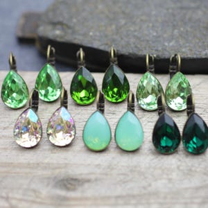 Puede incluir: Un conjunto de 10 pendientes en forma de lágrima con una variedad de piedras de vidrio verdes e iridiscentes. Los pendientes tienen un engaste de metal bronce.