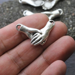 Può includere: Ciondolo in argento con due mani intrecciate, simbolo di amicizia o amore.