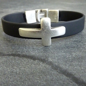 May include: Black rubber bracelet with a silver cross charm. The bracelet features a silver clasp and a cross-shaped centerpiece. The cross is made of a brushed metal, and the bracelet is a simple, yet elegant design.