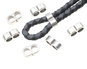 May include: Silver-toned metal beads with two holes each, designed for use with leather cord. The beads are arranged on a white surface, with one bead attached to a black leather cord.