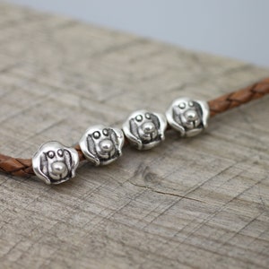 May include: Five silver dog head charms on a brown leather cord. The charms are detailed with a small nose and two eyes.