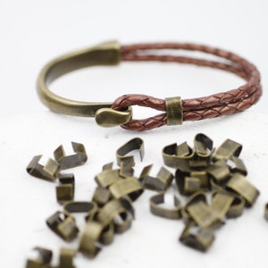 Peut inclure: Un bracelet en cuir marron avec un fermoir en m&eacute;tal et un embout en m&eacute;tal. Le bracelet est compos&eacute; de deux brins de cuir tress&eacute;s ensemble. Il y a aussi beaucoup de petits fermoirs en m&eacute;tal dans l'image.