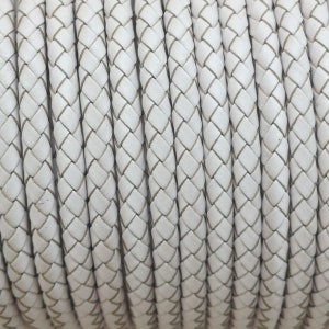 May include: Close-up of white braided leather cord. The cord is woven in a diamond pattern.