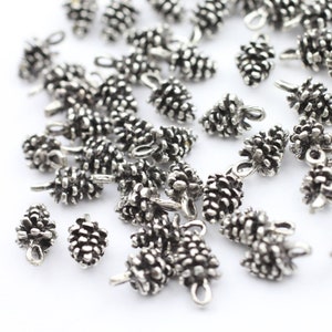 Könnte beinhalten: Eine Sammlung silberfarbener Metall-Kiefernzapfen-Anhänger mit einer Öse zum Anbringen an Schmuck oder andere Bastelarbeiten.