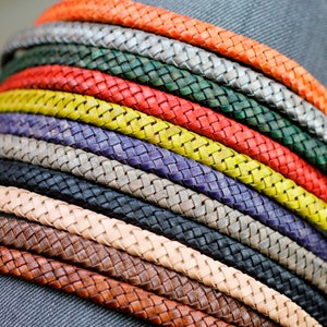Puede incluir: Una pila de cordones de cuero trenzados en varios colores, incluyendo negro, marrón, beige, gris, morado, amarillo, rojo y verde.