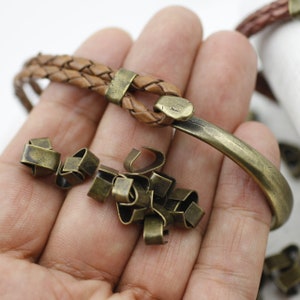 Peut inclure: Gros plan sur une main tenant un bracelet en cuir marron avec un fermoir en m&eacute;tal. Il y a aussi un tas de petits fermoirs en m&eacute;tal dans la main.