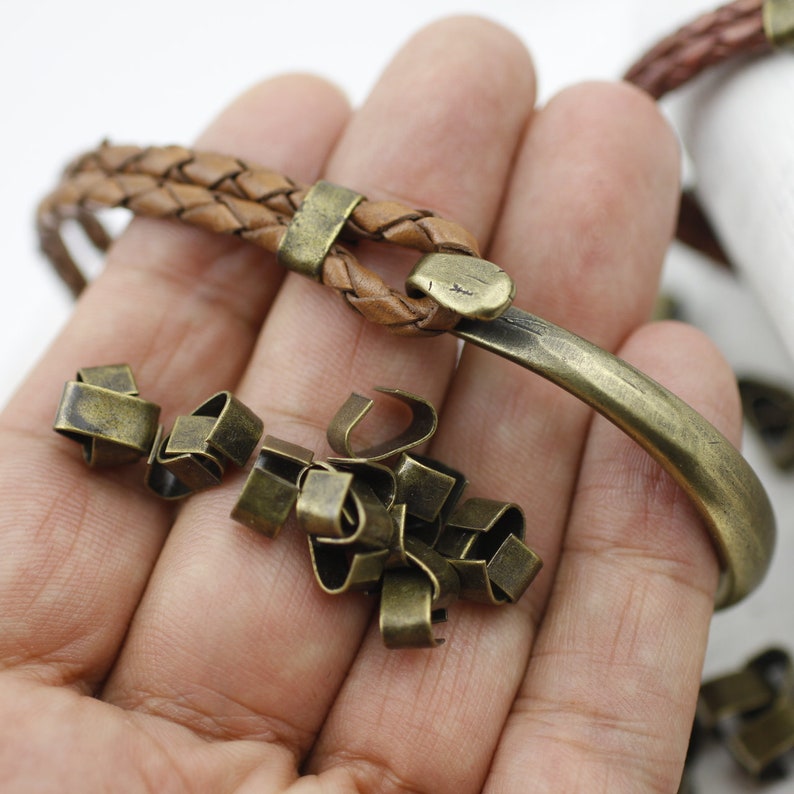 Peut inclure: Gros plan sur une main tenant un bracelet en cuir marron avec un fermoir en m&eacute;tal. Il y a aussi un tas de petits fermoirs en m&eacute;tal dans la main.