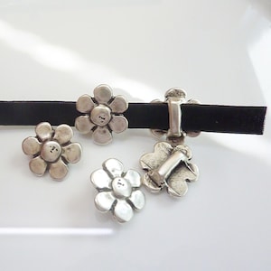 Peut inclure: Fermoirs et éléments décoratifs argentés en forme de fleur. Les fermoirs sont fixés à un ruban de velours noir. Les détails floraux ont un aspect rustique et antique. L'image est sur fond blanc.