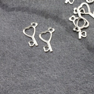 May include: Two silver key charms shaped like hearts with a keyhole and a small heart at the bottom.