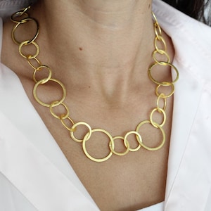 Puede incluir: Un collar de oro con grandes círculos entrelazados. El collar está hecho de un metal grueso y texturizado.