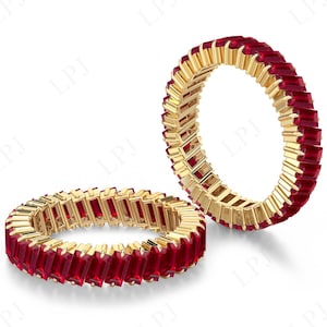 Peut inclure: Deux bagues d'éternité dorées avec des pierres précieuses rouges vibrantes. Les bagues sont présentées sur fond blanc, mettant en valeur le design complexe et le contraste des couleurs. Les pierres sont de coupe rectangulaire.