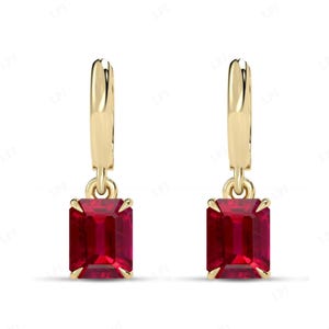 May include: A pair of gold-colored drop earrings with rectangular, deep red gemstones. The earrings have a simple, elegant design, with the gemstones securely set in a gold frame.