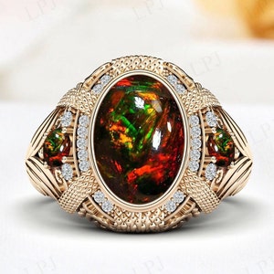 Op de afbeelding: Een gouden ring met een grote ovale edelsteen gezet in een gedetailleerd, sierlijk ontwerp. De edelsteen is een levendige mix van rood, oranje, groen en zwart.