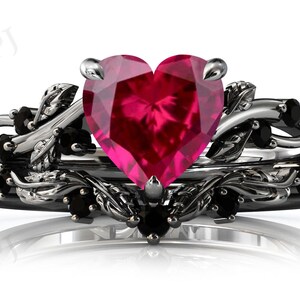 May include: A black and silver ring with a large heart-shaped ruby gemstone and smaller black gemstones set in a leafy design.