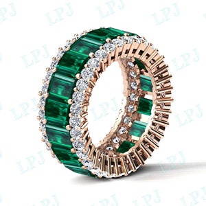 May include: A rose gold band ring with a row of emerald green baguette cut gemstones and a row of round brilliant cut diamonds.