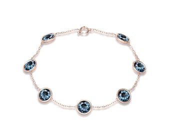 May include: A delicate rose gold bracelet featuring oval-cut, deep blue gemstones. The bracelet has a chain link design with eight evenly spaced stones. The clasp is a simple circular design. The jewelry is set against a white background.