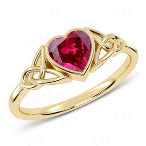 Puede incluir: Un anillo de oro con un diseño de nudo celta y una piedra preciosa en forma de corazón de rubí.