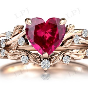 May include: A rose gold ring set with a large heart-shaped ruby and smaller diamonds set in a delicate vine design.