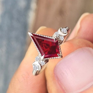 May include: A silver ring with a red gemstone in a kite shape and smaller diamonds set in a crescent moon design.