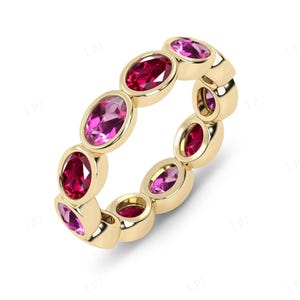 Op de afbeelding: Een gouden ring met afwisselende ovale edelstenen in roze en rood. De edelstenen zijn gezet in een doorlopende band, waardoor een volledig eternity ring ontwerp ontstaat. Het metaal van de ring heeft een gepolijste afwerking.