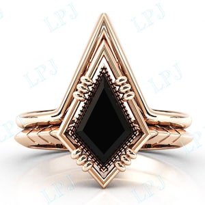 Może przedstawiać: Złoty pierścionek zaręczynowy z czarnym diamentem osadzonym w geometrycznym wzorze w kształcie strzały.