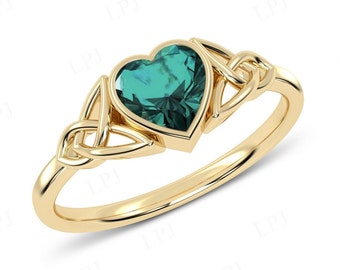 May include: A gold ring with a Celtic knot design and a heart-shaped emerald green gemstone.