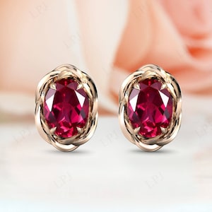 May include: A pair of gold earrings with a red gemstone in the centre of each earring. The earrings are set in a delicate, twisted design.