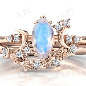 May include: A rose gold ring set with a large marquise-shaped moonstone and smaller round diamonds. The ring features a delicate floral design with crescent moons and small flowers.