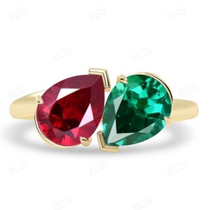 May include: A gold ring with a pear-shaped ruby and a pear-shaped emerald gemstone. The gemstones are set in a way that they appear to be intertwined.