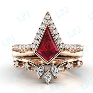 May include: A rose gold ring set with a large, red, faceted gemstone in a triangular setting. The ring is surrounded by smaller, clear gemstones. The ring is a delicate and elegant piece of jewelry.