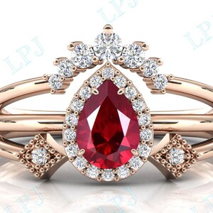 May include: A pear-shaped ruby gemstone ring with a halo of smaller diamonds. The ring is set in rose gold and has a delicate crown-like design above the ruby.