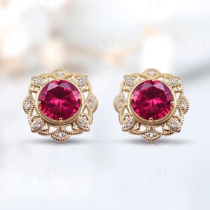 Puede incluir: Un par de pendientes de oro con una piedra preciosa roja rodeada de piedras blancas más pequeñas en un diseño floral.