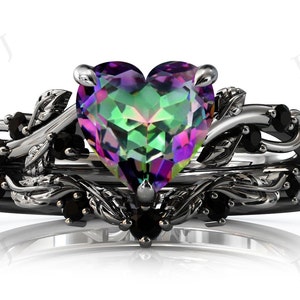 May include: A heart-shaped, iridescent gemstone ring set in a silver band with black gemstones and a delicate, leafy design.