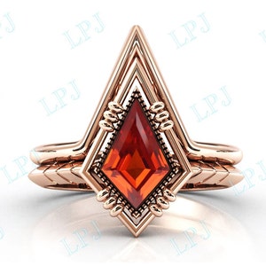 May include: A rose gold ring with a geometric design featuring a large, red, faceted gemstone. The ring has a double band with a chevron pattern.