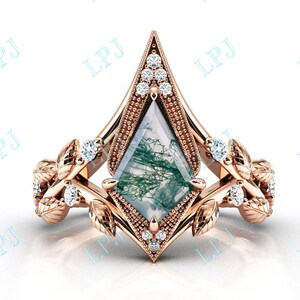 Puede incluir: Un anillo de oro rosa con una piedra preciosa de ágata verde musgo engastada en un engaste puntiagudo en forma de diamante. El anillo está adornado con delicados acentos de hojas a cada lado de la piedra preciosa, adornados con pequeños diamantes transparentes.
