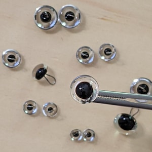 May include: Assortment of clear plastic safety eyes with black pupils, some with metal posts, for craft projects.