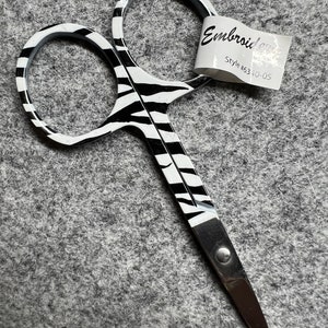 May include: Black and white zebra patterned embroidery scissors with a silver handle. The scissors have a label that reads "Embroidery Style #6340-05".