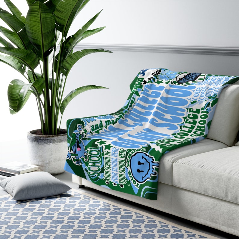Peut inclure: Une couverture bleue, verte et blanche drap&eacute;e sur un canap&eacute; blanc. La couverture pr&eacute;sente les mots "COLLEGE SCHOOL" et "YOUR SCHOOL HERE" dans un motif r&eacute;p&eacute;titif. Le design comprend des graphiques de dessins anim&eacute;s et des &eacute;toiles.