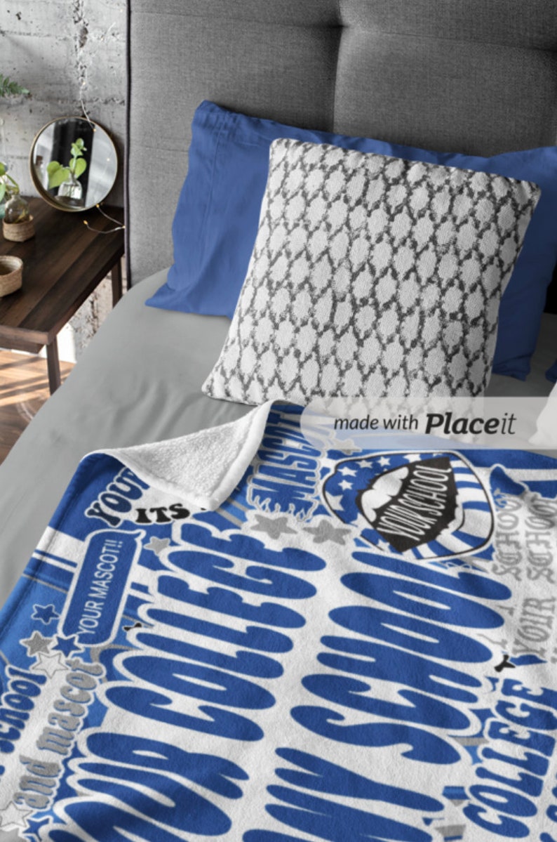 Peut inclure: Une couverture bleue et blanche sur le th&egrave;me du coll&egrave;ge avec le texte "YOUR SCHOOL" et "COLLEGE" dans une police stylis&eacute;e. La couverture pr&eacute;sente un motif d'&eacute;toile et de bouclier. Un oreiller &agrave; motifs et des oreillers bleus reposent sur un lit gris.