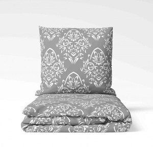 Può includere: Set di biancheria da letto grigio e bianco con un cuscino. La biancheria da letto ha un motivo damascato.